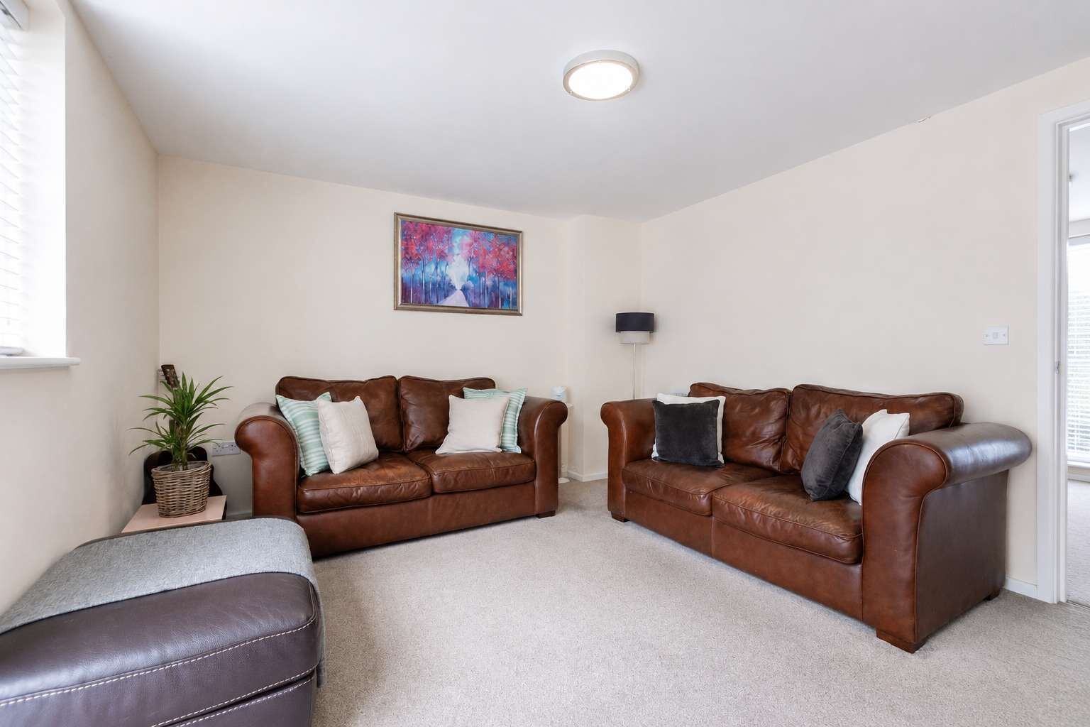 A living room with two brown leather sofas, a grey ottoman, a floor lamp, and a painting on the wall.