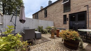 Eine Terrasse mit Korbmöbeln, Topfpflanzen und einem Backsteinhaus im Hintergrund.