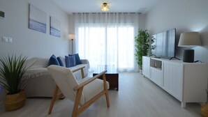 Ein modernes Wohnzimmer mit Sofa, Sessel, Fernseher und einer Pflanze.
