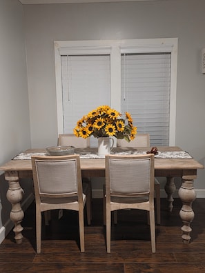 Ein Esstisch mit einer Sonnenblumenvase, zwei Stühlen und einem Fenster mit Jalousien.