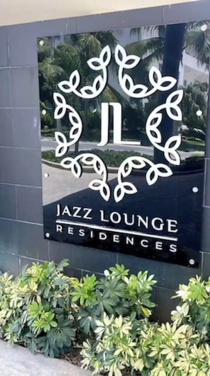 Señalización de 'Jazz Lounge Residences' con un emblema decorativo y vista a zonas verdes.