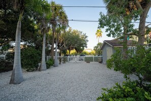 A gravel driveway leading to a gated entrance, surrounded by palm trees and a white fence. - Romantic Beachfront Studio for 2 Unit B (Indian Rocks Beach)