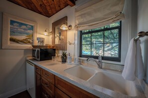 A kitchen with a double sink, wooden cabinets, a microwave, a coffee maker, and a window with a view of trees. - Romantic Beachfront Studio for 2 Unit B (Indian Rocks Beach)
