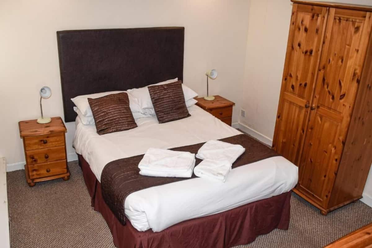 A bed with a dark headboard, two bedside tables with lamps, a wooden wardrobe, and a brown carpet.