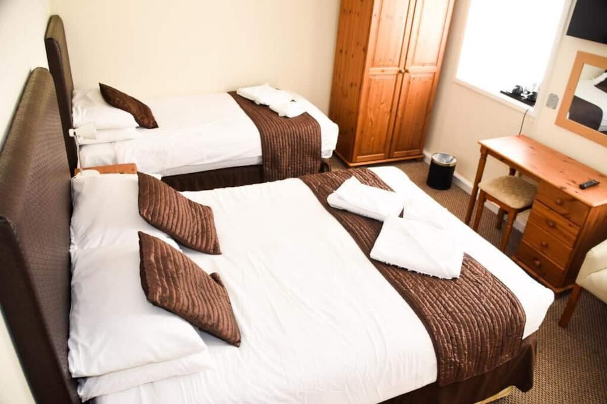 A hotel room with two beds, a wooden wardrobe, a desk, and a chair.
