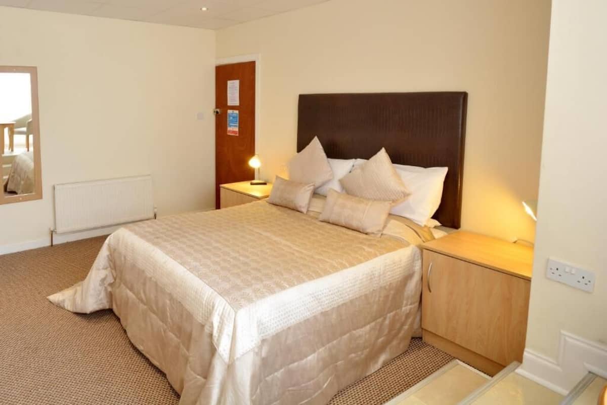 A hotel room with a bed, bedside tables, a wooden headboard, a radiator, and a door with a notice.