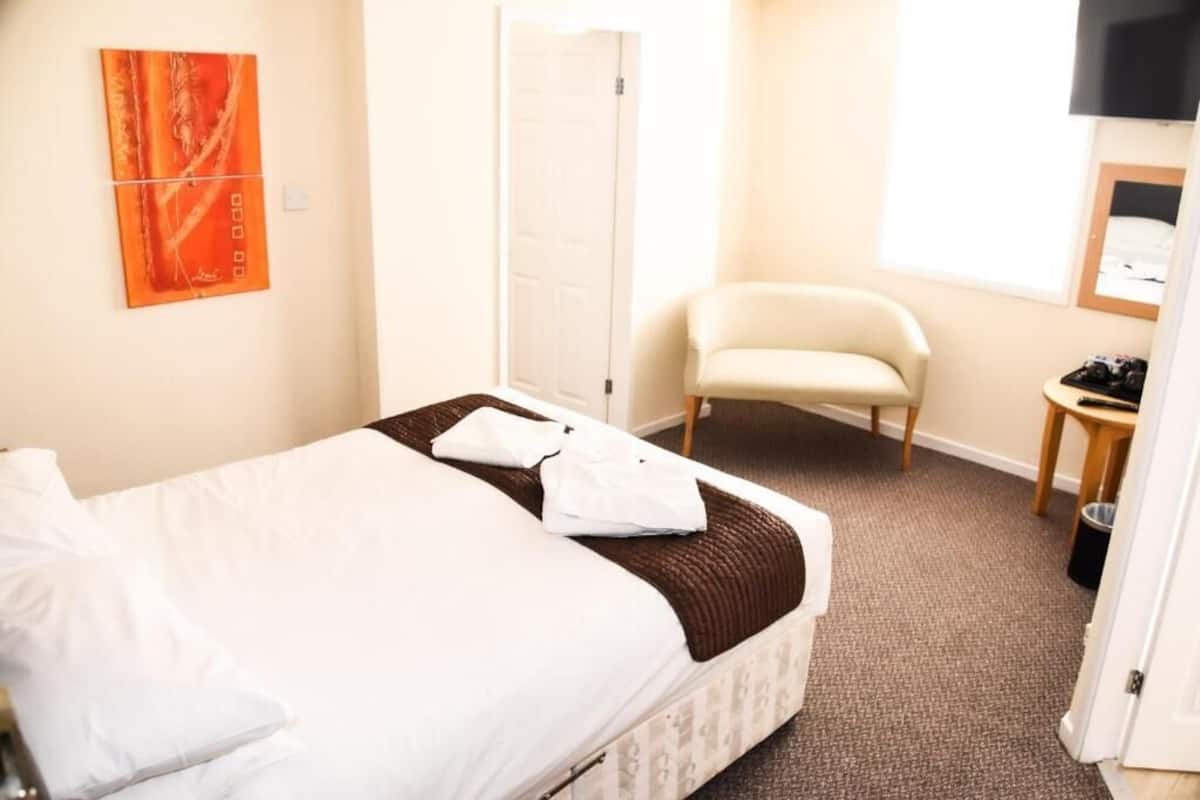 A hotel room with a bed, a chair, a small table, and a TV mounted on the wall.