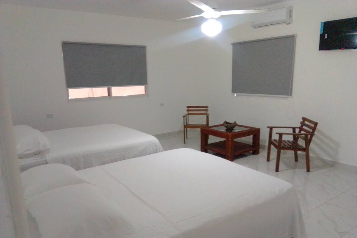 A room with two single beds, a wooden table with chairs, and a ceiling fan.