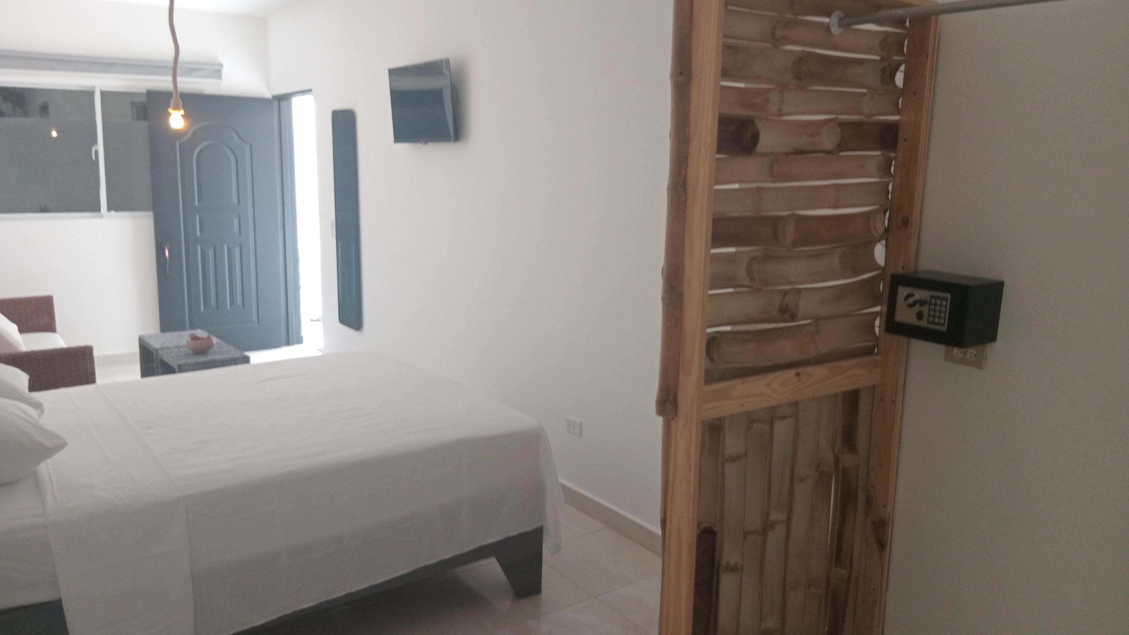 Un dormitorio con cama, un separador de madera, una puerta y un termostato fijado a la pared.