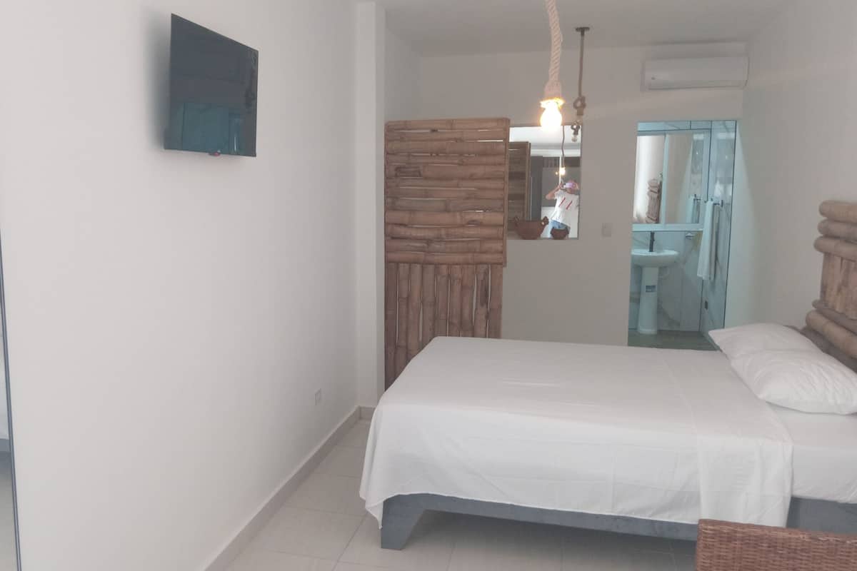 A bedroom with a bed, a mirror, a wall-mounted TV, and a wooden partition.