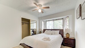 A bedroom with a bed, a ceiling fan, a nightstand, a mirror, and a window with curtains. - Family Pool Retreat in Spring , Houston  4BR Private Pool  Sleeps 8 (Spring)