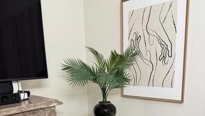 A television on a marble fireplace, a wooden side table with a plant, and a framed abstract art piece on the wall. - Family Villa with Jacuzzi, Large Garden & Free Parking (Quinta do Conde)