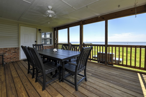 A covered outdoor deck with a table and chairs, a ceiling fan, and a view of the ocean.