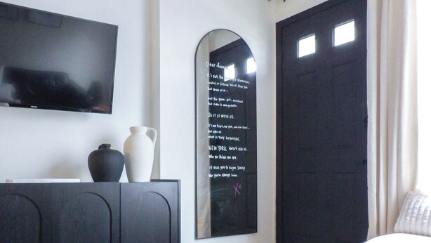 Una sala moderna con un televisor de pantalla plana, una mesa de centro de vidrio, un sofá oscuro, un sillón blanco y una puerta negra.