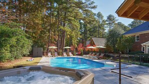 A swimming pool with a hot tub, lounge chairs, and umbrellas.