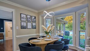 A dining area with a round table, six chairs, and a chandelier.