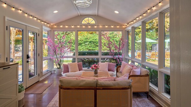 A covered patio with a seating area, large windows, and a ceiling light fixture.