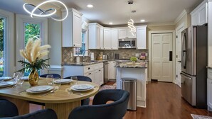 A modern kitchen with white cabinets, stainless steel appliances, and a dining area with a round table and chairs.