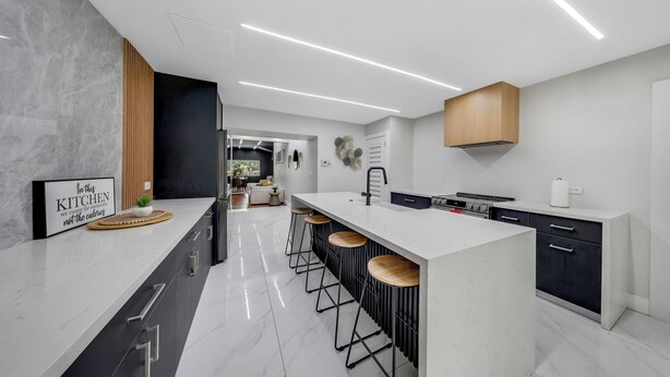 Une cuisine moderne avec un plan de travail blanc, des meubles de rangement noirs et un îlot central doté de tabourets.