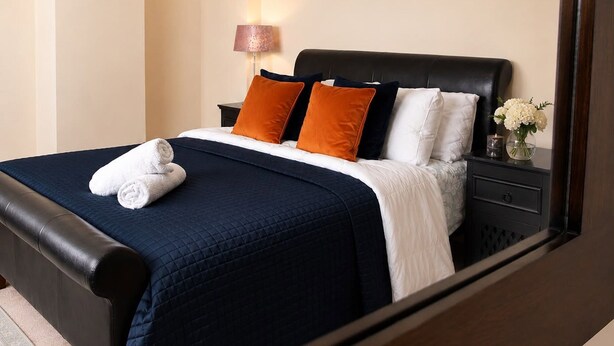A neatly made bed with a dark blue bedspread, white and orange pillows, and a rolled white towel. - Spacious 3BR Hartlepool Stay | Contractor Friendly (Hartlepool)