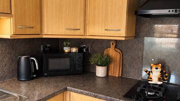 A kitchen with wooden cabinets, a microwave, a kettle, a small potted plant, a cutting board, and a stove.