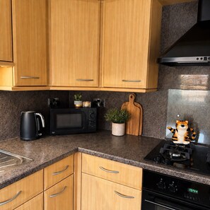 A kitchen with wooden cabinets, a microwave, a kettle, a small potted plant, a cutting board, and a stove.