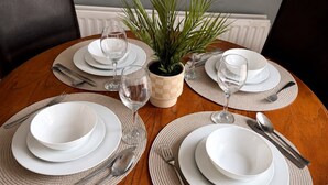 A round dining table with white plates, cutlery, and glassware, surrounded by woven placemats and a potted plant. - Spacious 3BR Hartlepool Stay | Contractor Friendly (Hartlepool)