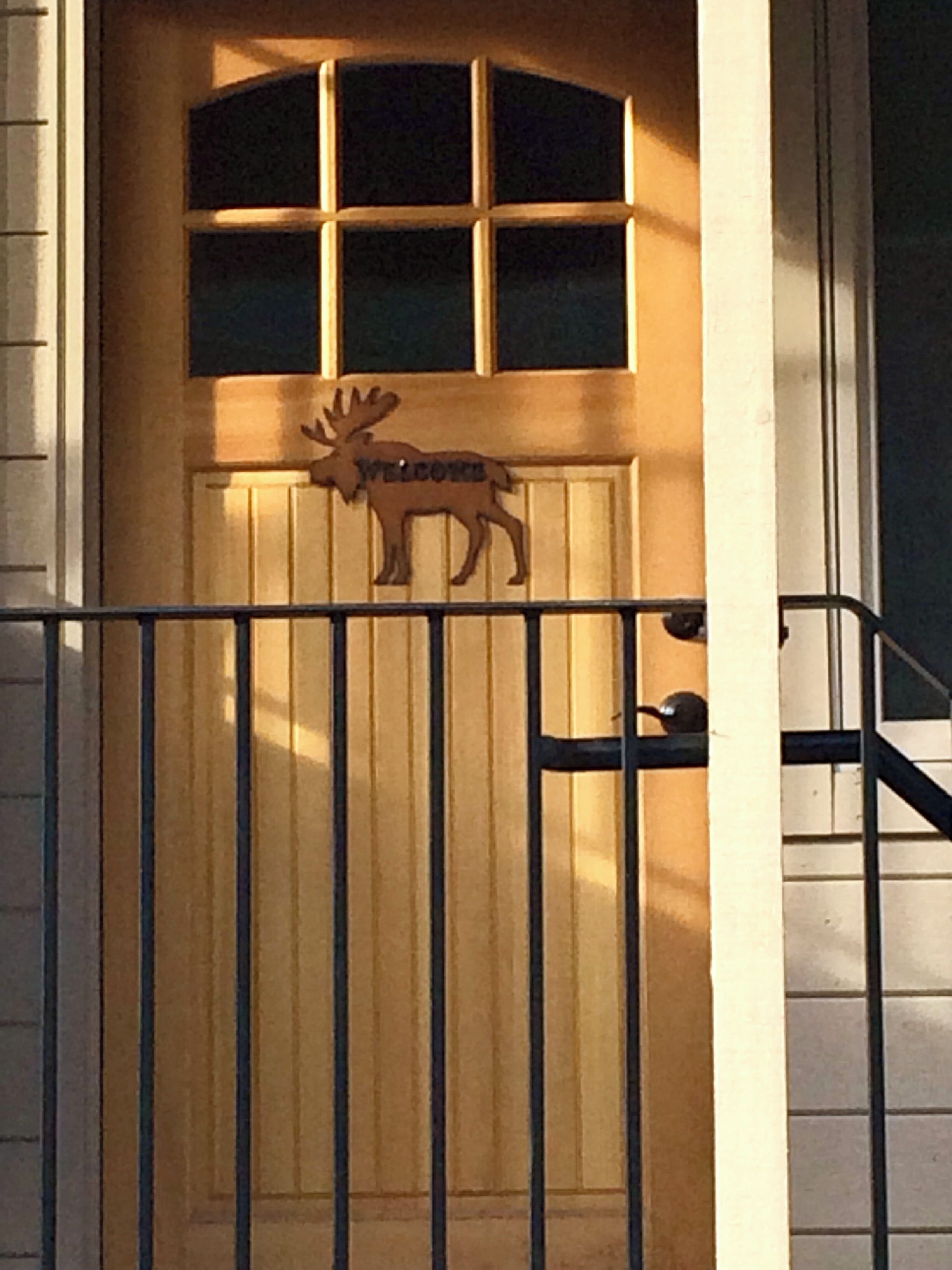 Een houten deur met een decoratie van een eland en het woord 'WELCOME' erboven.