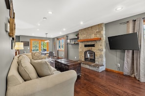 A living room with a stone fireplace, a flat-screen TV mounted on the wall, and a sofa.