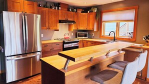 A modern kitchen with wooden cabinets, stainless steel appliances, a central island, and a view of the outside.