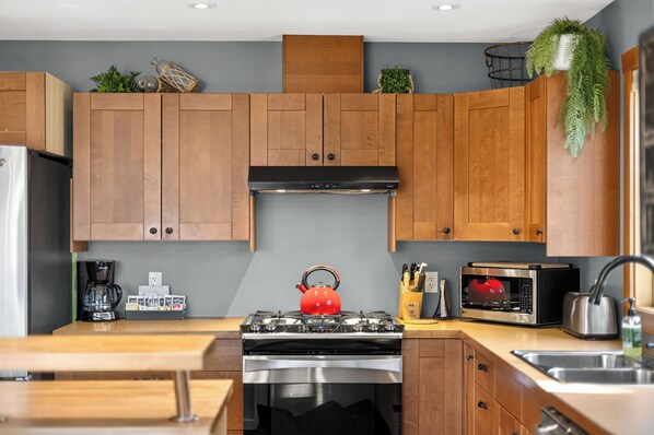 A modern kitchen with wooden cabinets, a gas stove, a red kettle, a coffee maker, and a microwave.
