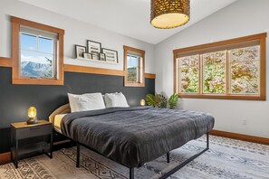 A bedroom with a bed, bedside tables, a lamp, a window with a view, and a wall-mounted shelf with pictures.