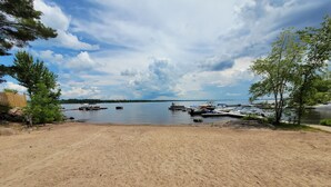 A sandy beach with boats docked in the water, trees, and a clear sky. - Maple Cabin at Pine Ridge Park (Pembroke)