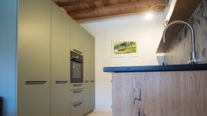 A modern kitchen with built-in appliances, wooden cabinets, and a single hanging light fixture. - Appartements - N°5 et N°5B by Interhome (Les Genevez)