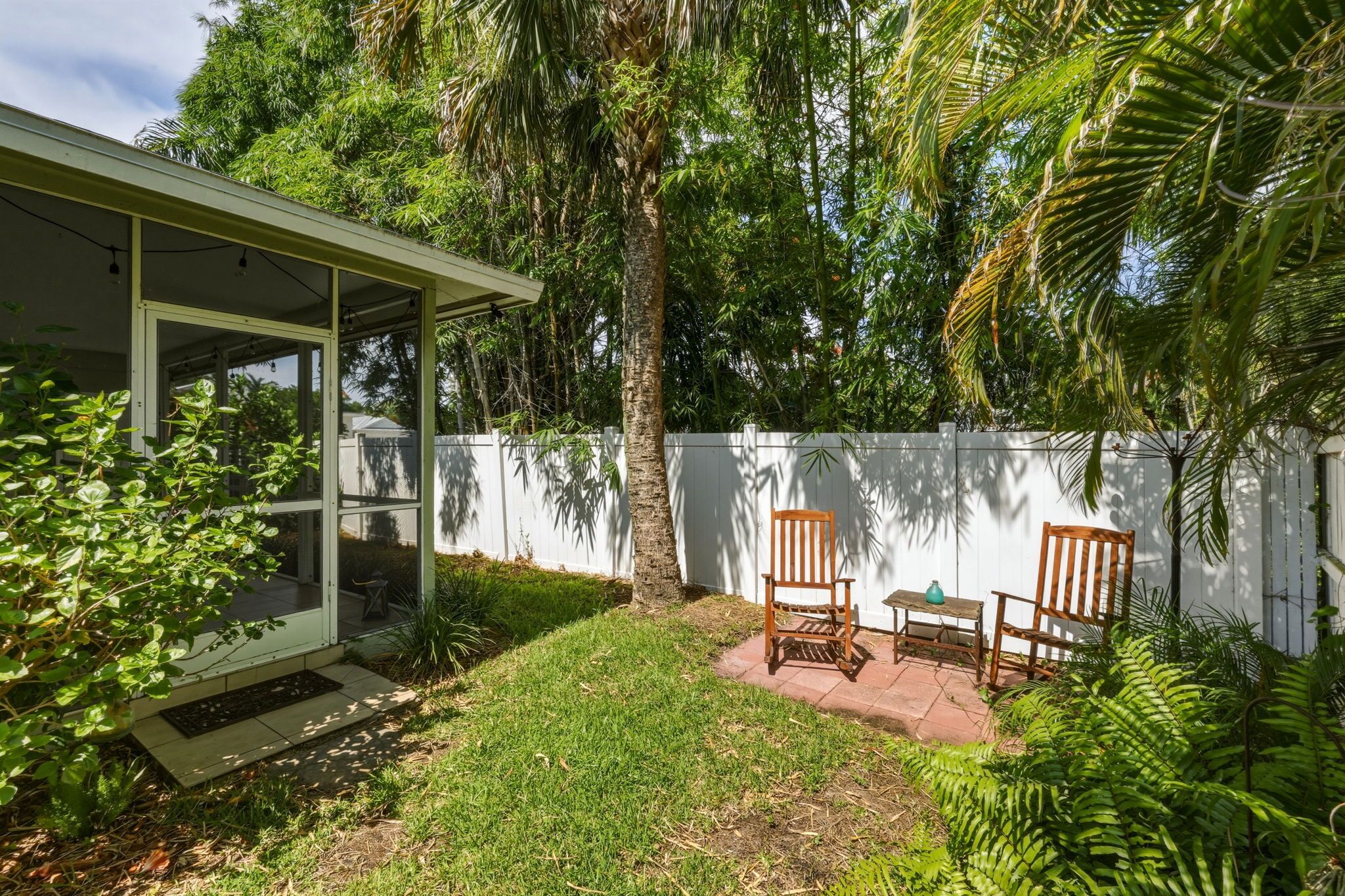 Une terrasse couverte avec une chaise en bois, une petite table et une clôture blanche.