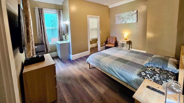 A bedroom with a bed, a television, a desk, a chair, and a window with curtains. - Ringgold (Providence)