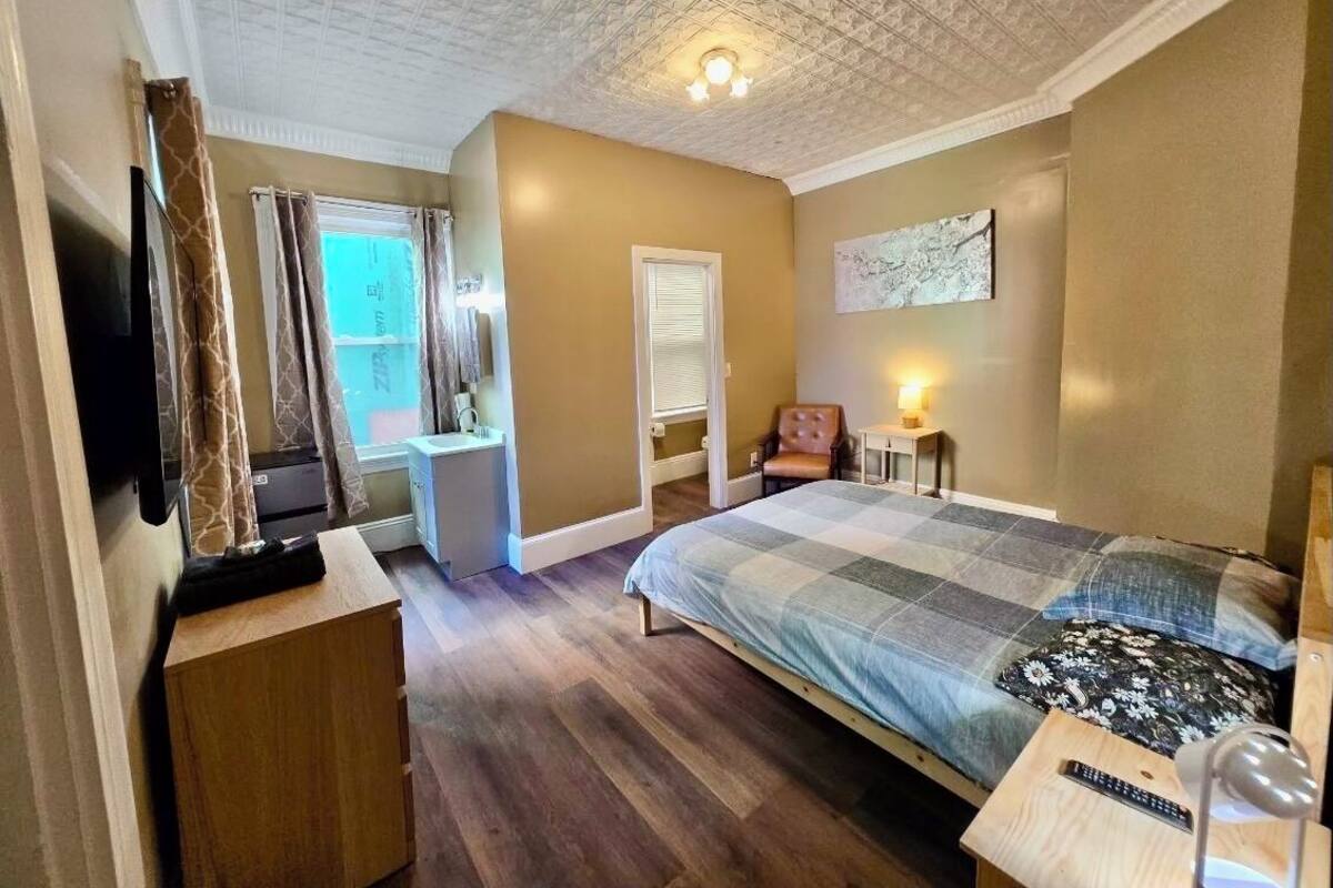 Une chambre à coucher avec un lit, une télévision, un bureau, une chaise et une fenêtre avec des rideaux.