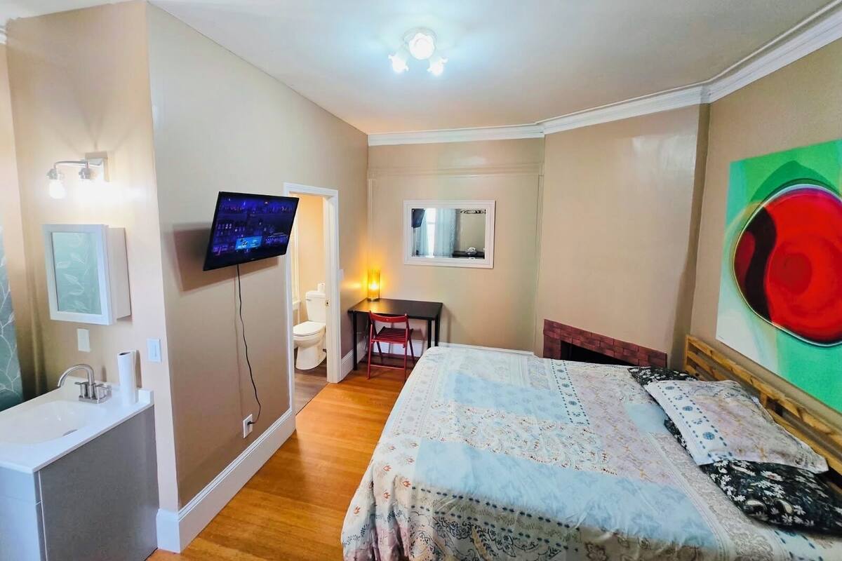Une chambre à coucher comprenant un lit, un bureau, une chaise, une télévision, un miroir et une cheminée.