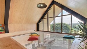 Ein modernes Interieur mit schrägem Dach, großen Fenstern und einem Glastisch mit Kissen.