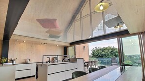 Eine moderne Küche mit einer langen Arbeitsplatte, einem Essbereich mit Stühlen und Blick durch große Fenster.