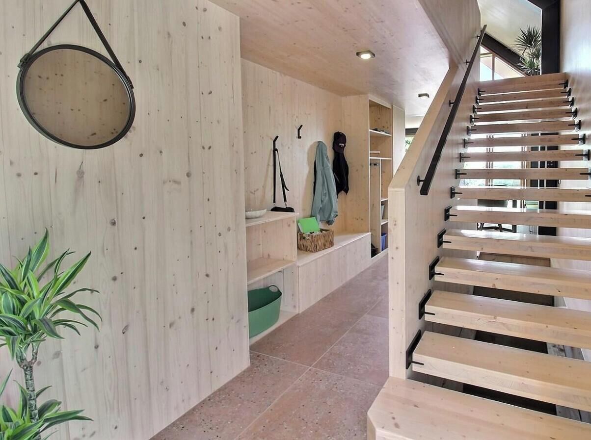 A wooden staircase with a handrail, a hanging light fixture, and a plant in a corner.