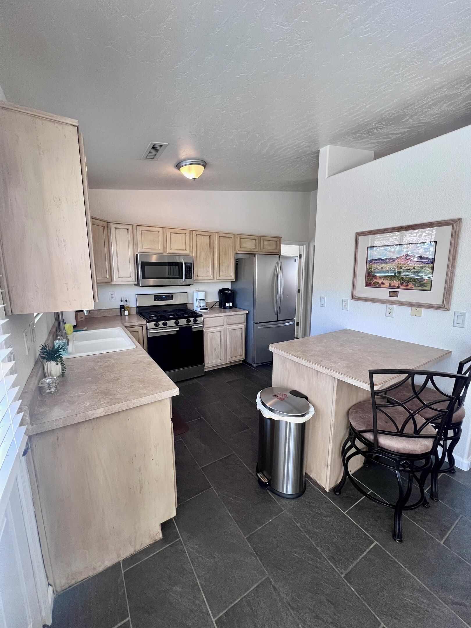 A kitchen with wooden cabinets, stainless steel appliances, a sink, and a trash can.