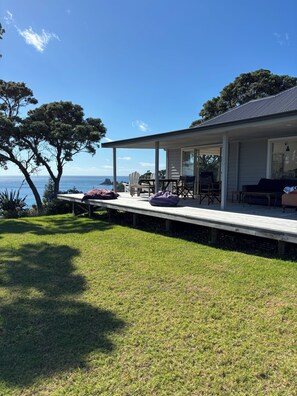 A covered outdoor area with a view of the sea, a wooden deck, and outdoor furniture. - Gorgeous Whananaki bach with stunning sea views - walk to the beach & estuary. (Whananaki)