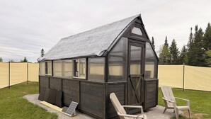Pieni puinen varasto, jossa on kalteva katto ja ovi, ja sen ympärillä on keltainen aita. Varaston ulkopuolella on kaksi tuolia.
