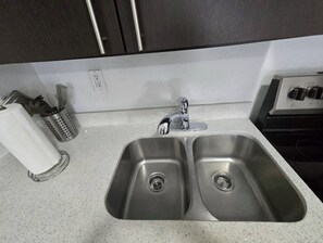 Uma cozinha com duas pias de aço inoxidável, um dispensador de papel toalha e um ralador de aço inoxidável.