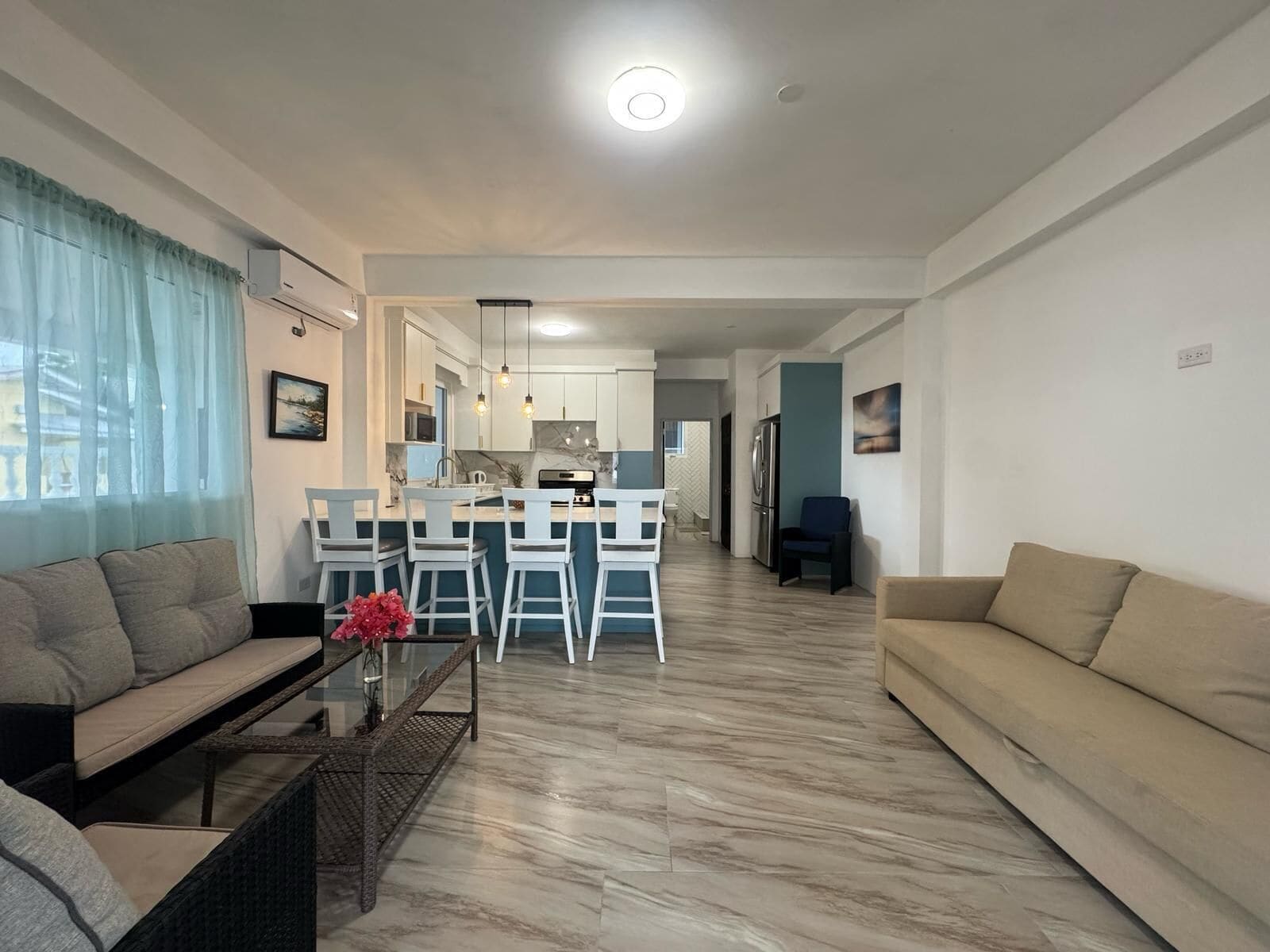 A modern living room with a sofa, a coffee table, and a dining area with bar stools.