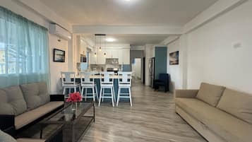 A modern living room with a sofa, a coffee table, and a dining area with bar stools.