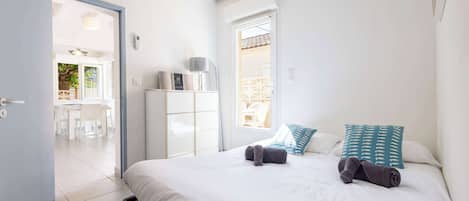 Un dormitorio con cama, almohadas, una mesita de noche, un armario y una puerta que da a un balcón.