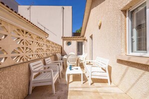 Eine Terrasse mit weißen Kunststoffmöbeln, einem kleinen Tisch und einer Zierwand.