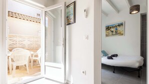 A room with a bed, a door leading to a balcony, a painting on the wall, and a ceiling light fixture. - Le Patio de la Mer – Comfortable one-bedroom flat with terrace in Valras-Plage (Valras-Plage)